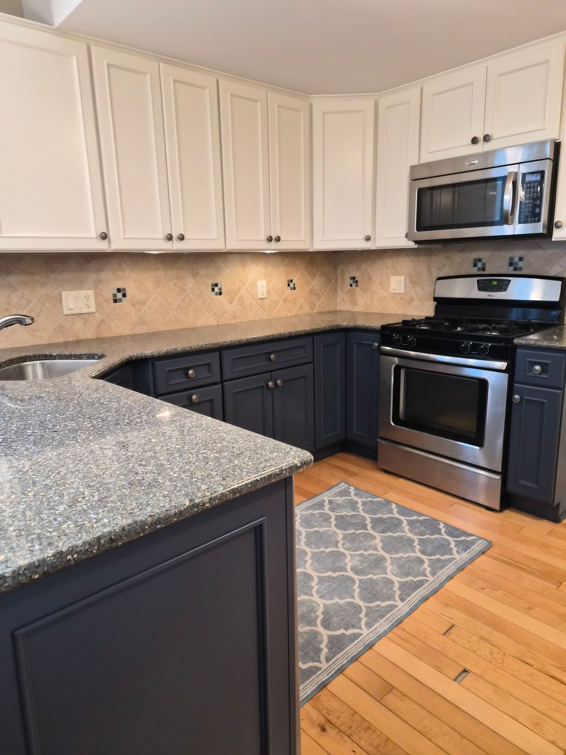 Kitchen with white upper cabinets and navy blue lower cabinets, granite countertops, and stainless steel appliances.
