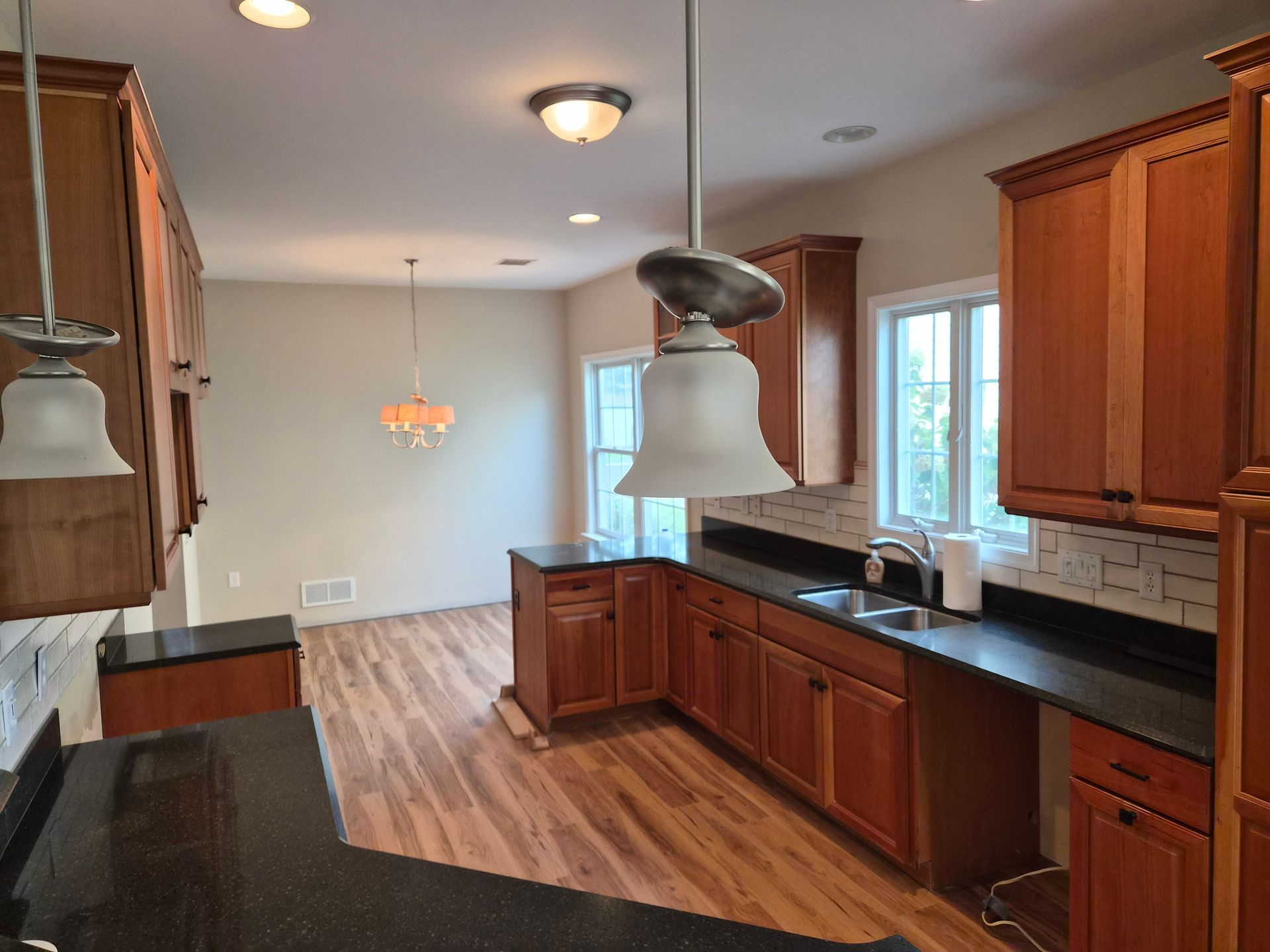 Kitchen with wood cabinets, black countertops, and pendant lights, neutral walls, and wood-look flooring.
