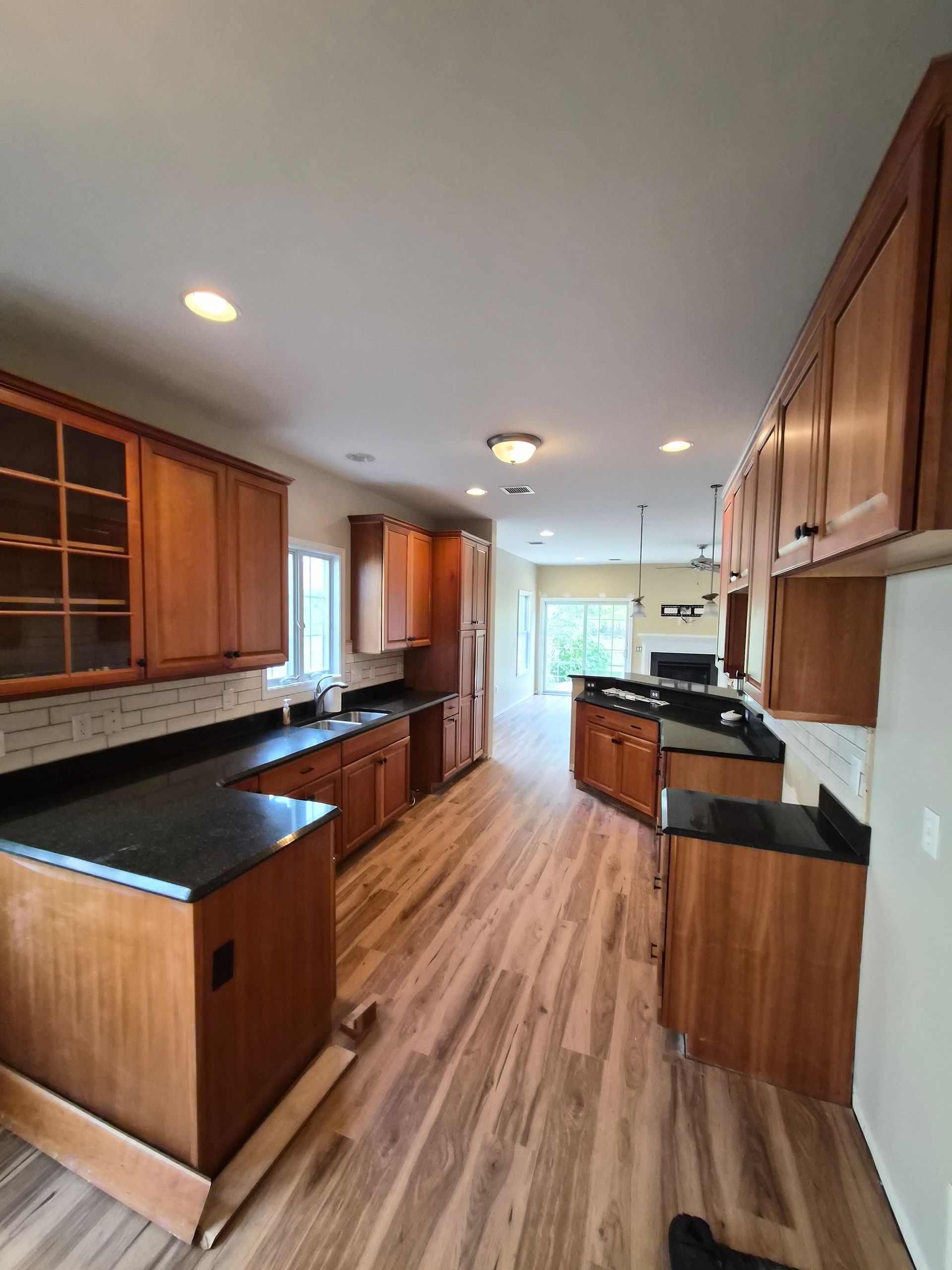 Long, narrow kitchen with wood cabinets, dark countertops, and light wood flooring.