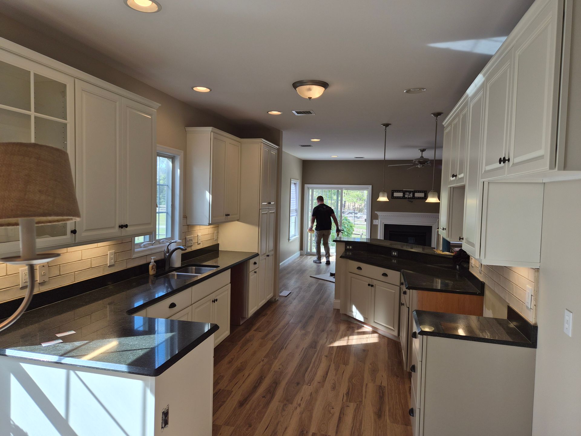 Newly renovated kitchen with white cabinets, dark countertops, and a person near a sliding door.