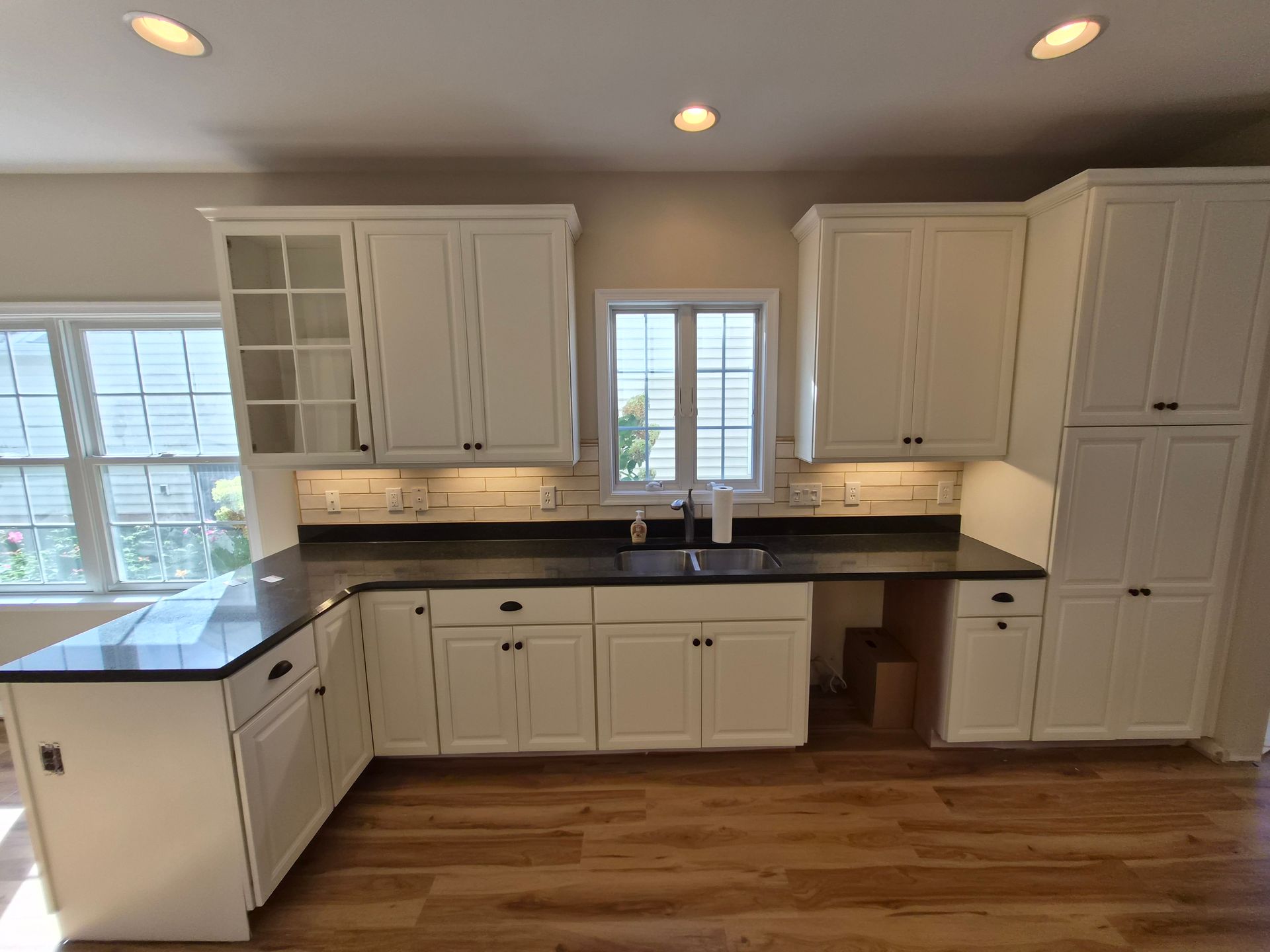 L-shaped kitchen with white cabinets, dark countertops, a window, and hardwood floors.
