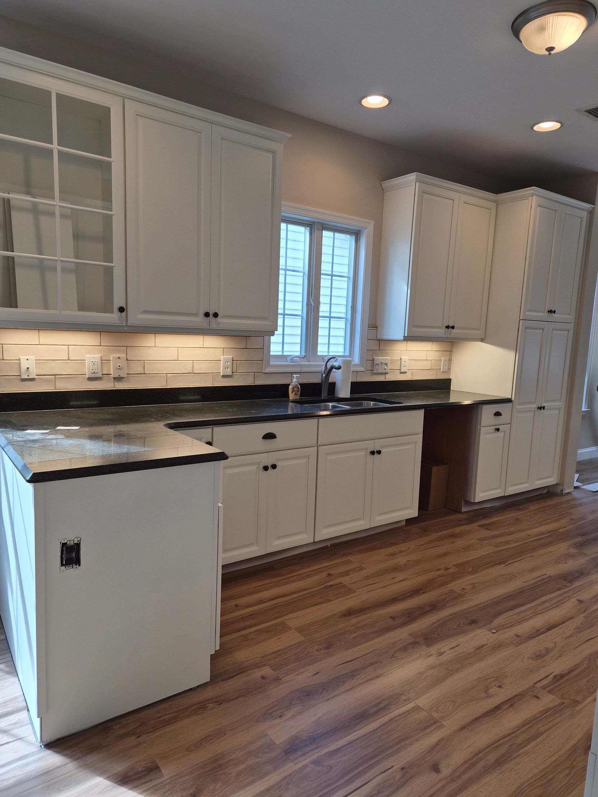 White kitchen cabinets, black countertops, and wooden floor. Window above sink.