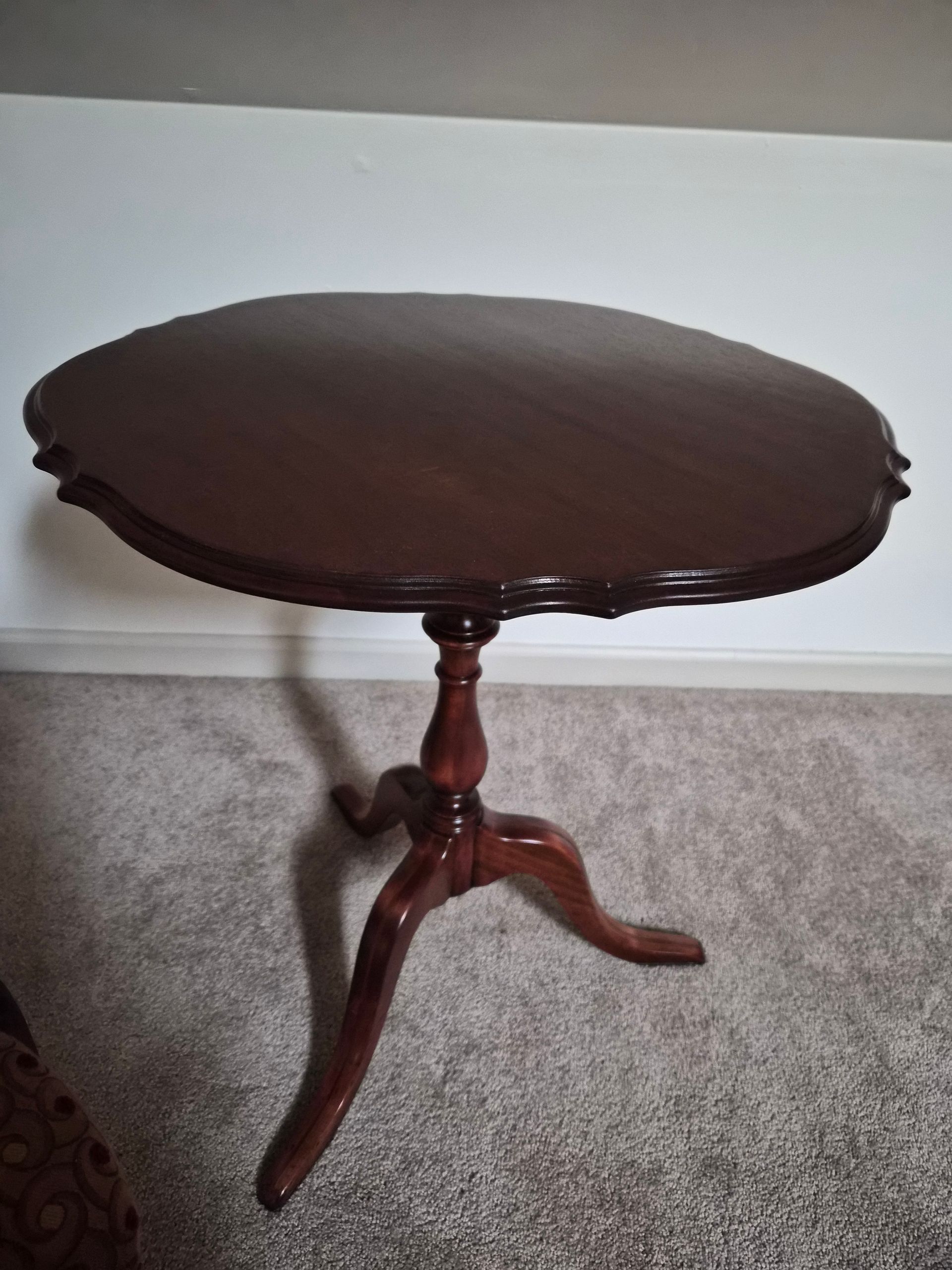 Dark wood, round side table with scalloped edge, on a three-legged base.