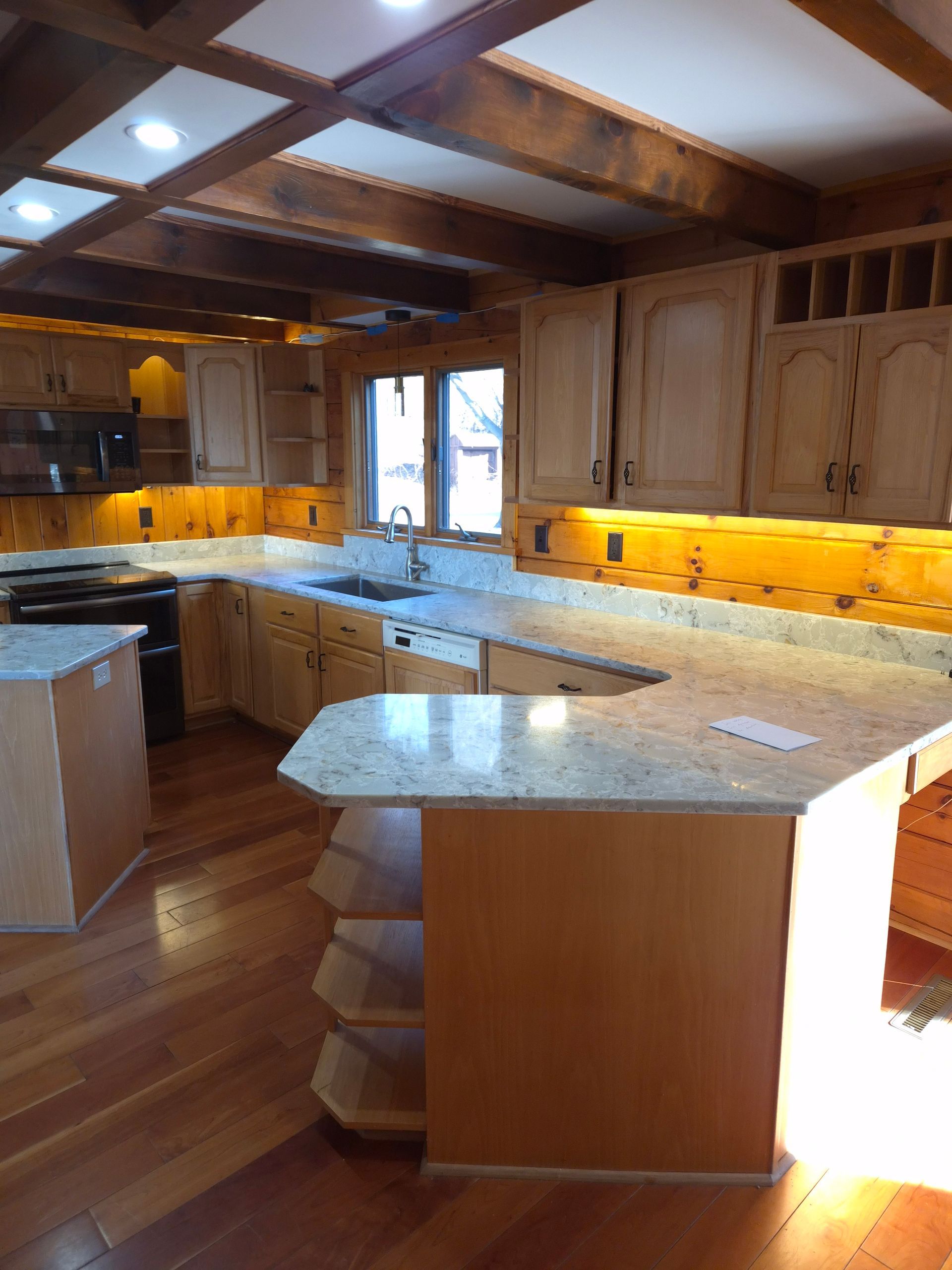 Kitchen with light-colored cabinets, granite countertops, and wooden beams. The floor is hardwood.
