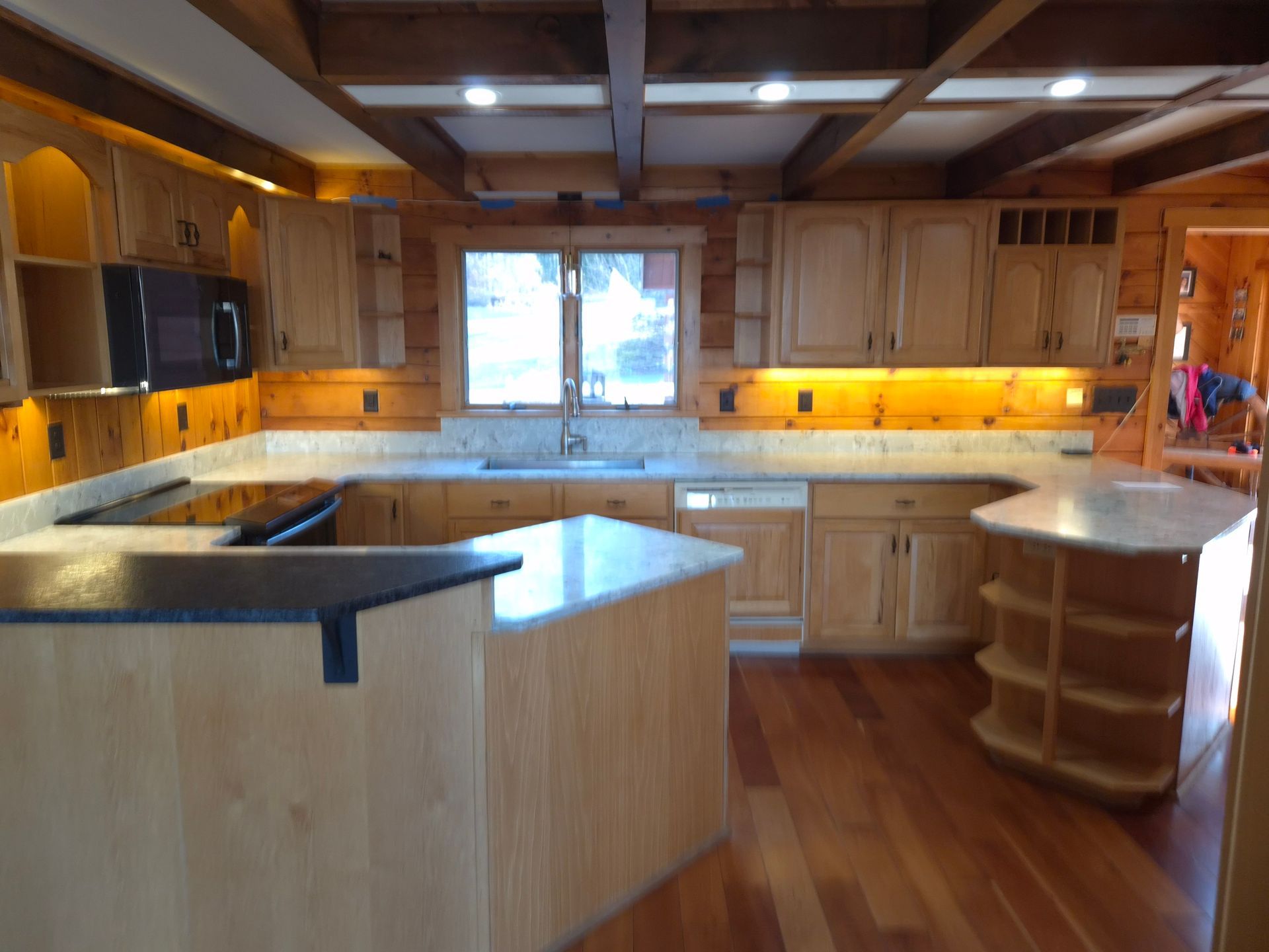 Kitchen with light wood cabinets, granite countertops, and wood flooring. Includes a microwave, island, and sink.