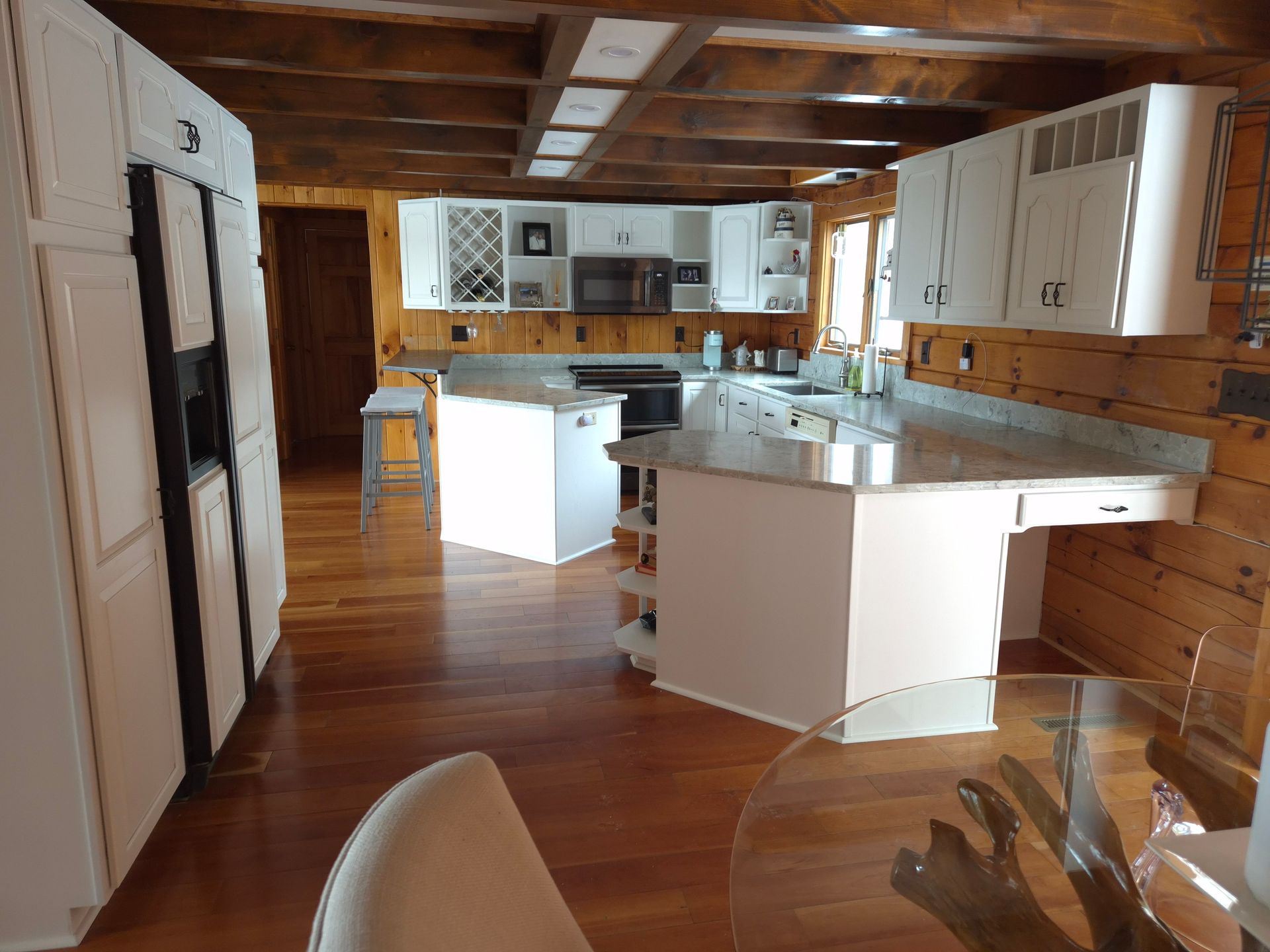 The kitchen with white cabinets, wooden floors, and countertops includes a large refrigerator.