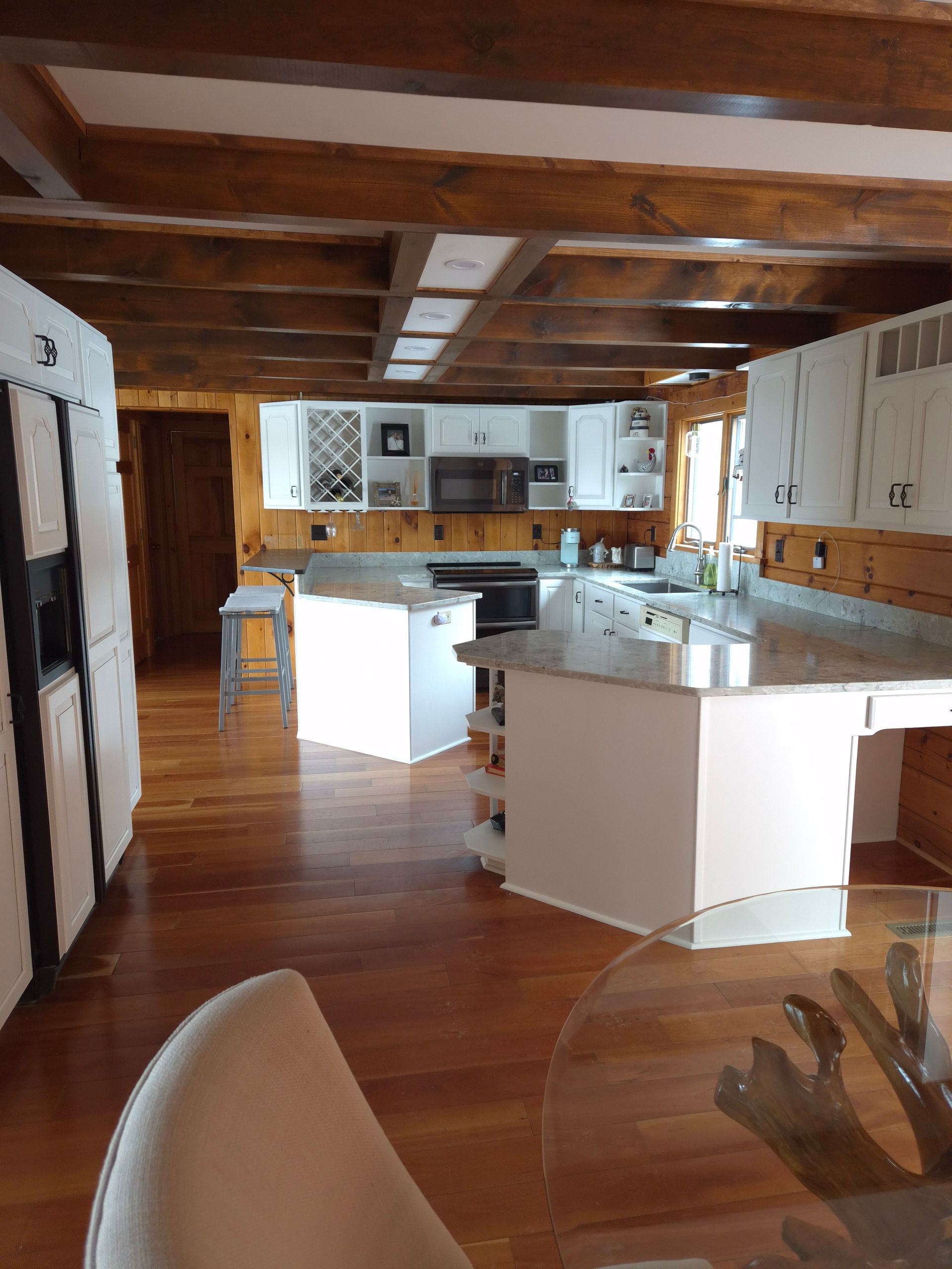 Spacious kitchen with wood floors and exposed beams, white cabinets, islands, and stainless steel appliances.
