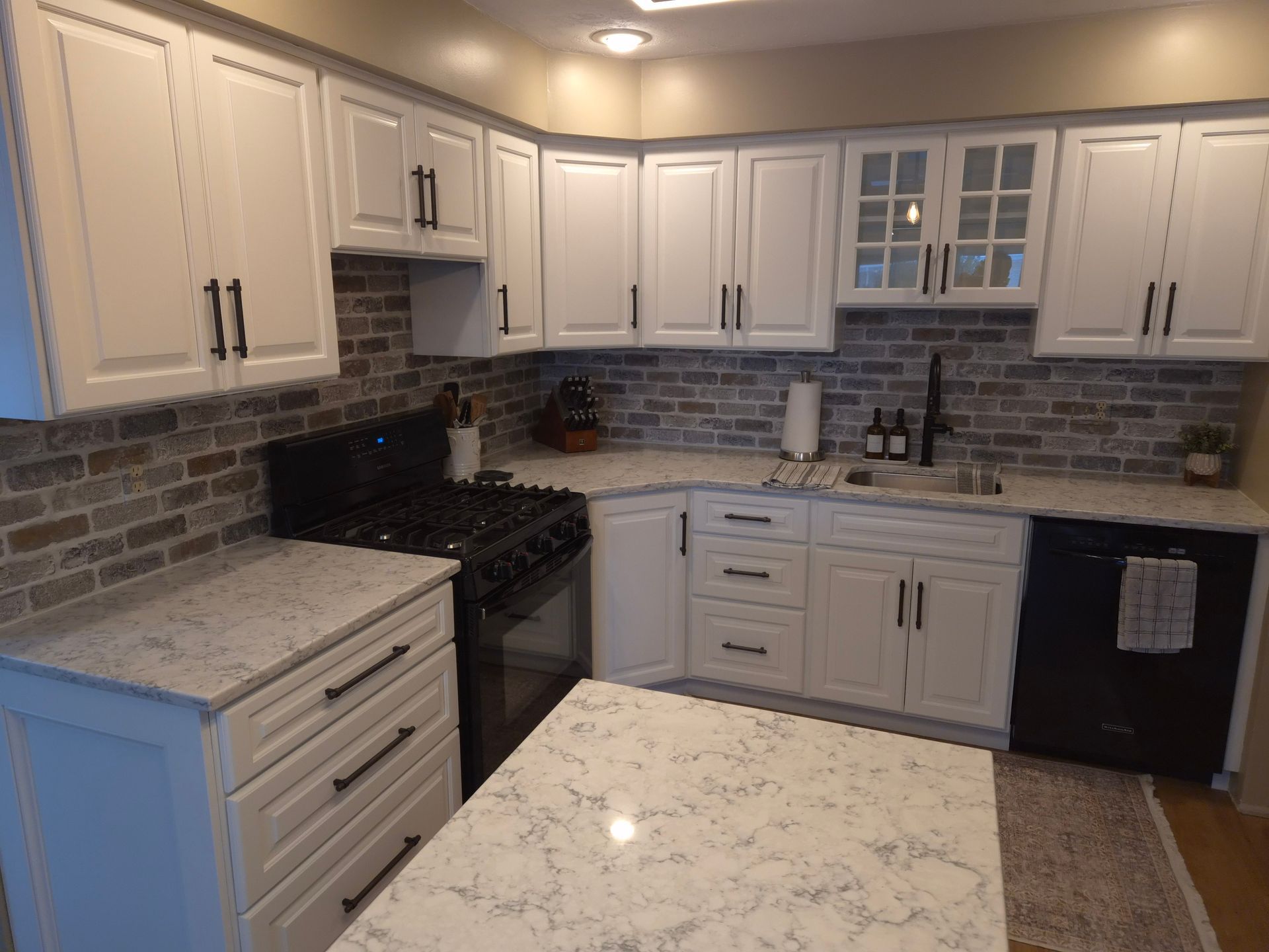 White kitchen cabinets with black hardware, a brick backsplash, and a countertop island.
