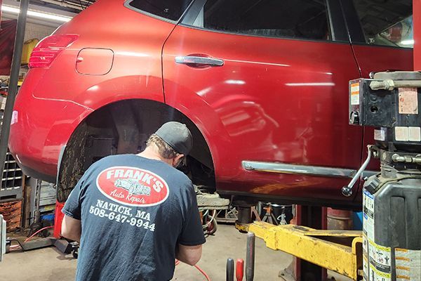 A man wearing a frank 's auto shirt is working on a red car