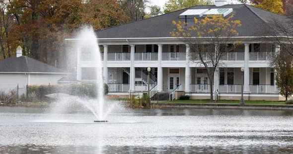 There is a fountain in the middle of a lake in front of a house.