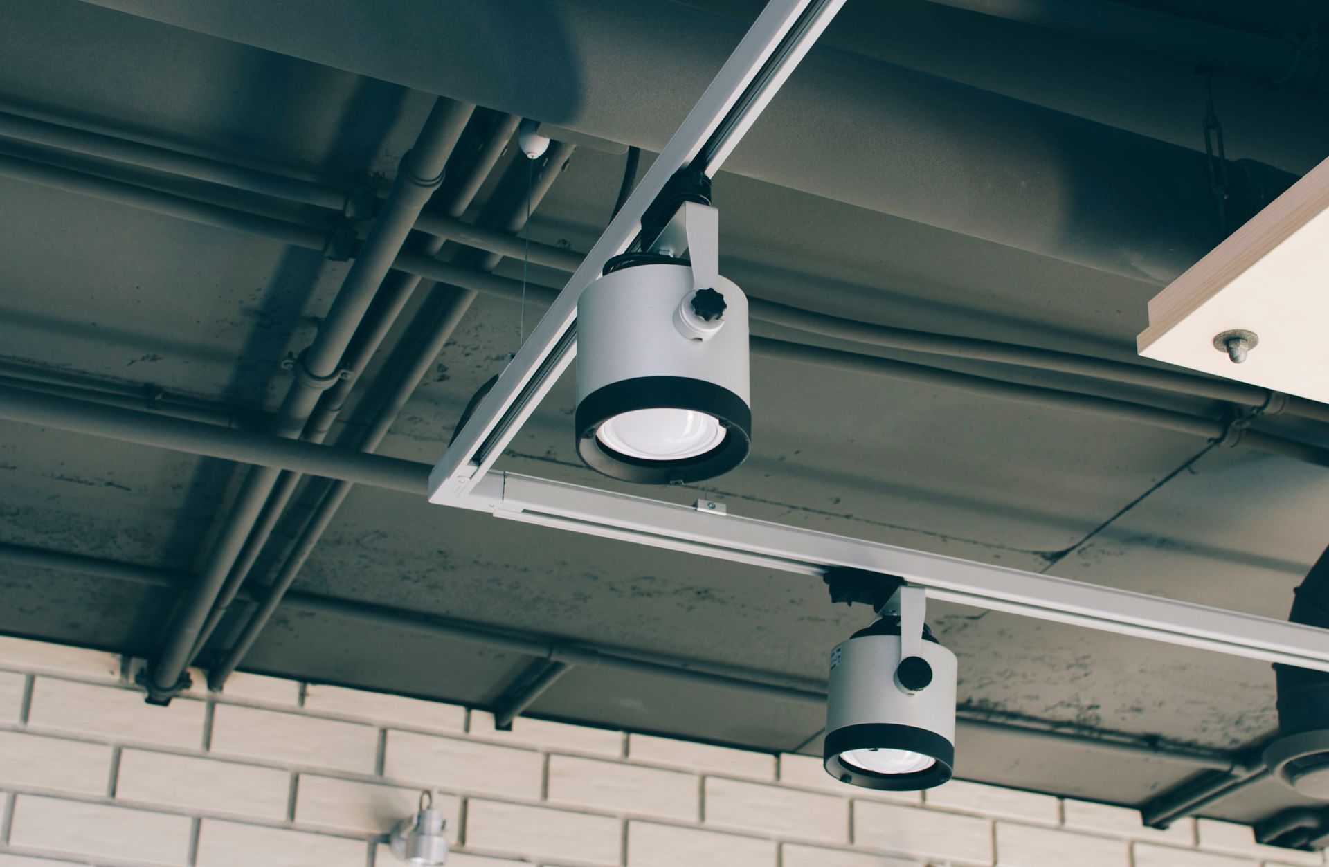 Ceiling-mounted security cameras on a warehouse ceiling with exposed pipes and brick wall