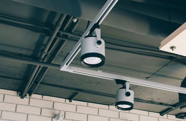 Ceiling-mounted security cameras on a warehouse ceiling with exposed pipes and brick wall