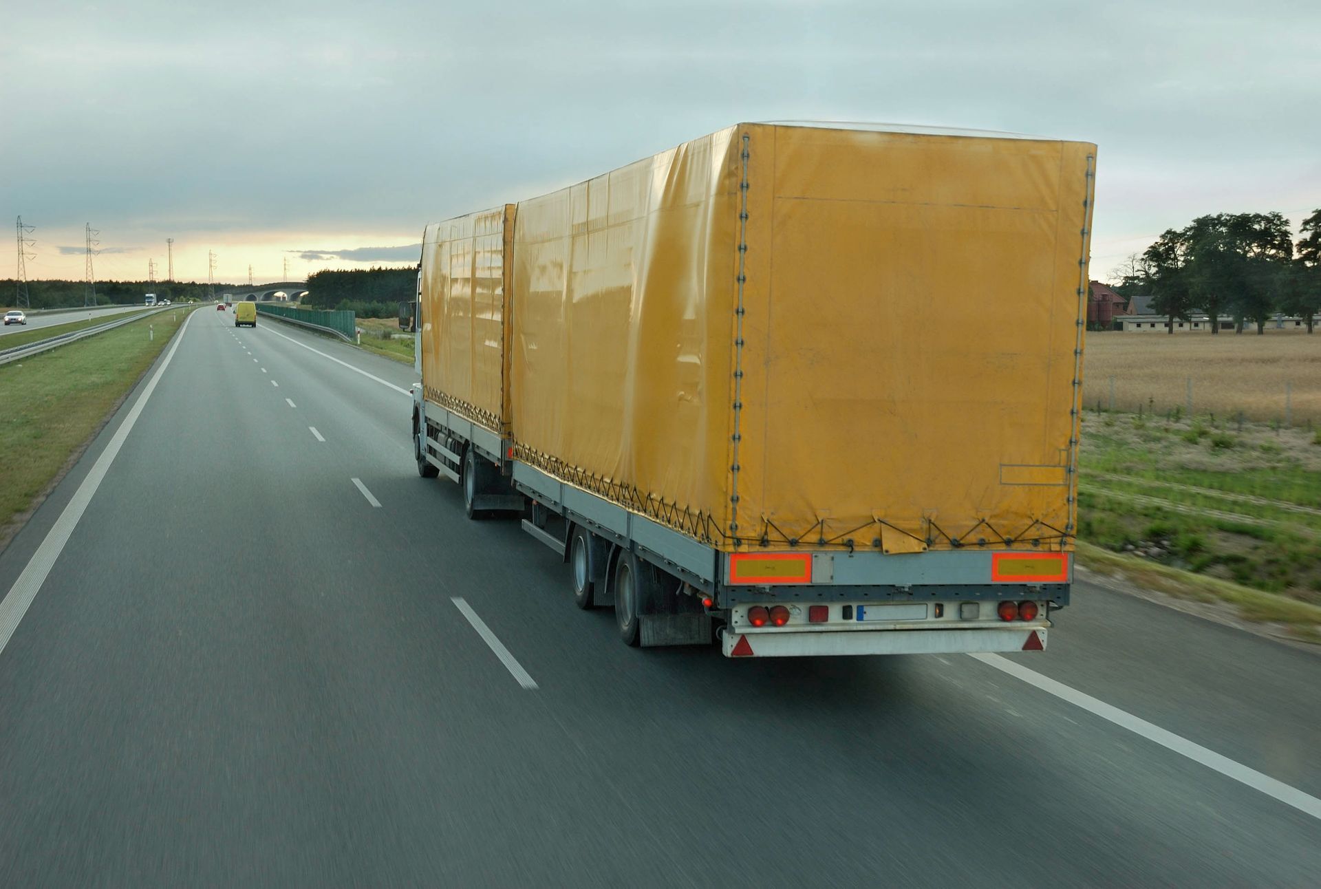 Yellow semi-truck with two trailers driving on a highway with fields on the side.