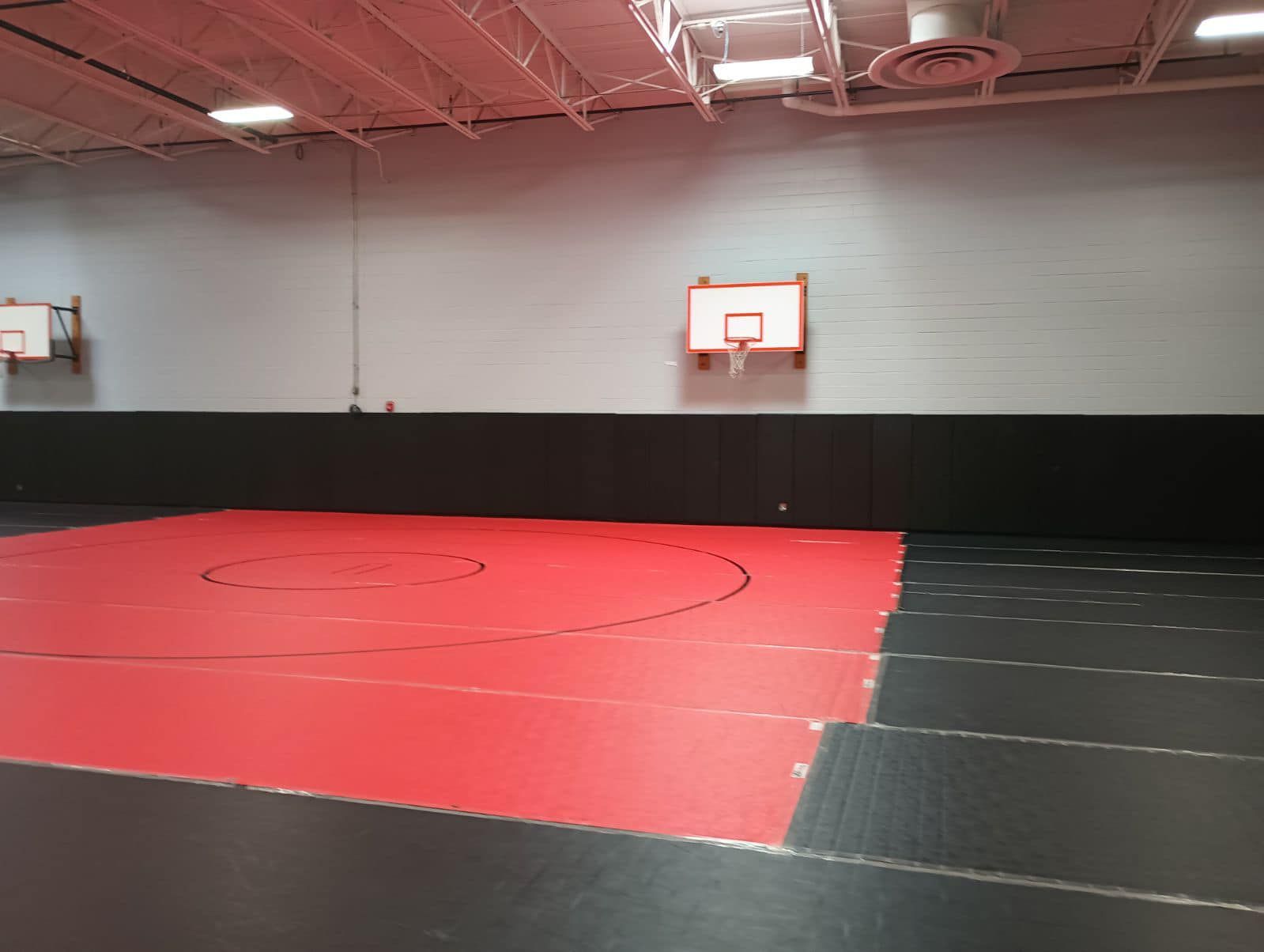 Wrestling/martial arts practice room with red and black mats, two mini basketball hoops.
