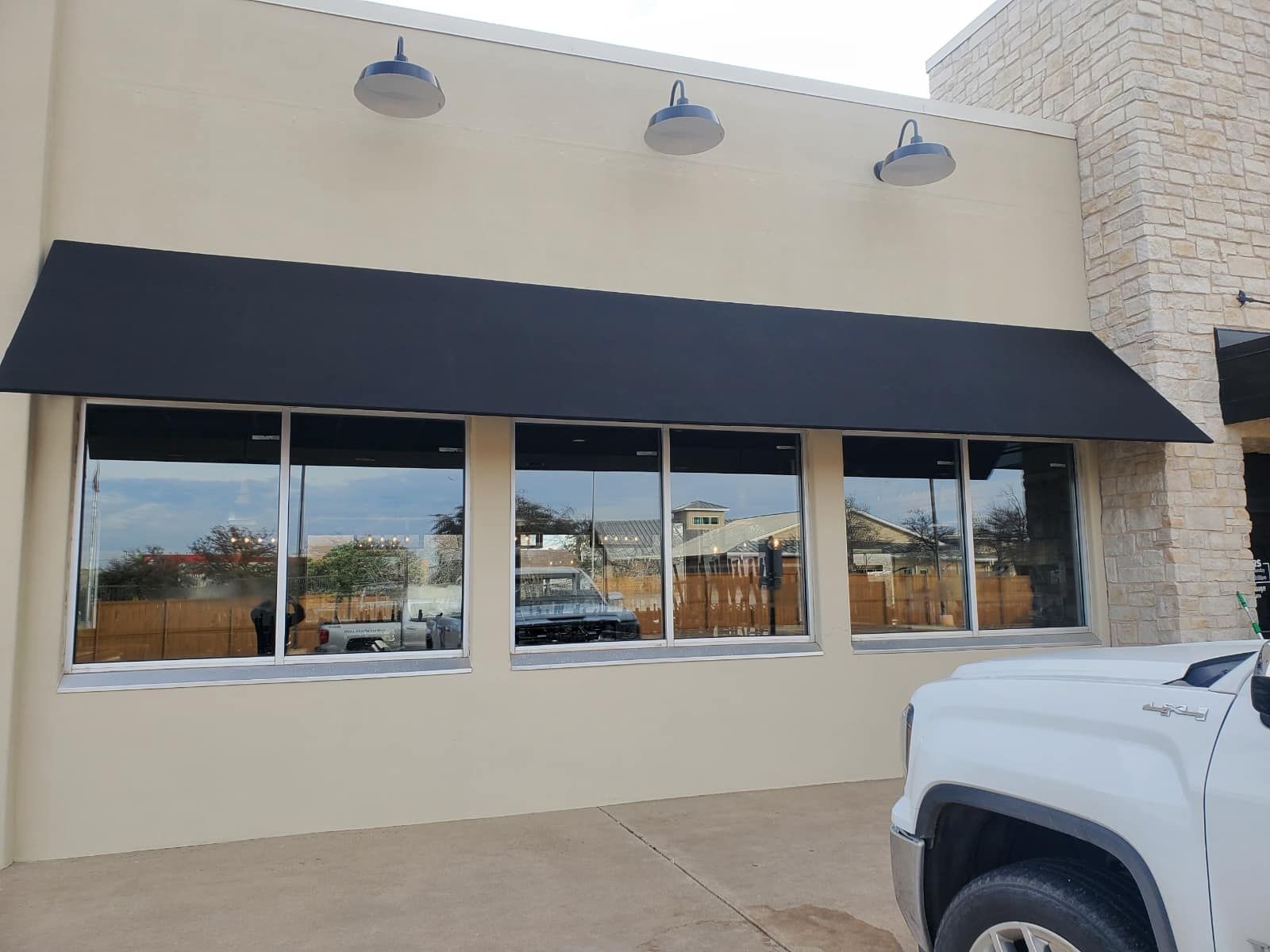 Exterior of a building with a black awning over large windows.  A white truck is parked in front.