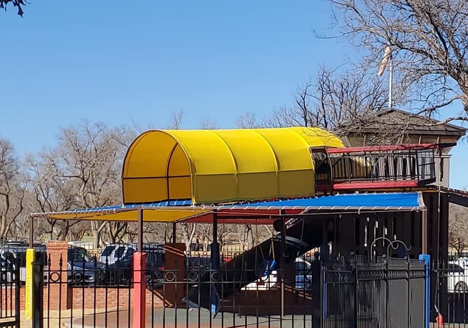 Playground with yellow canopy and blue roof, behind a black fence.