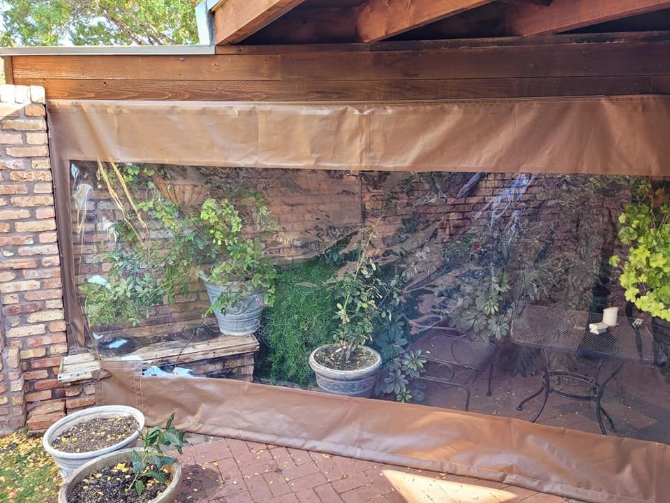 Clear vinyl outdoor screen protects plants in a brick patio area.