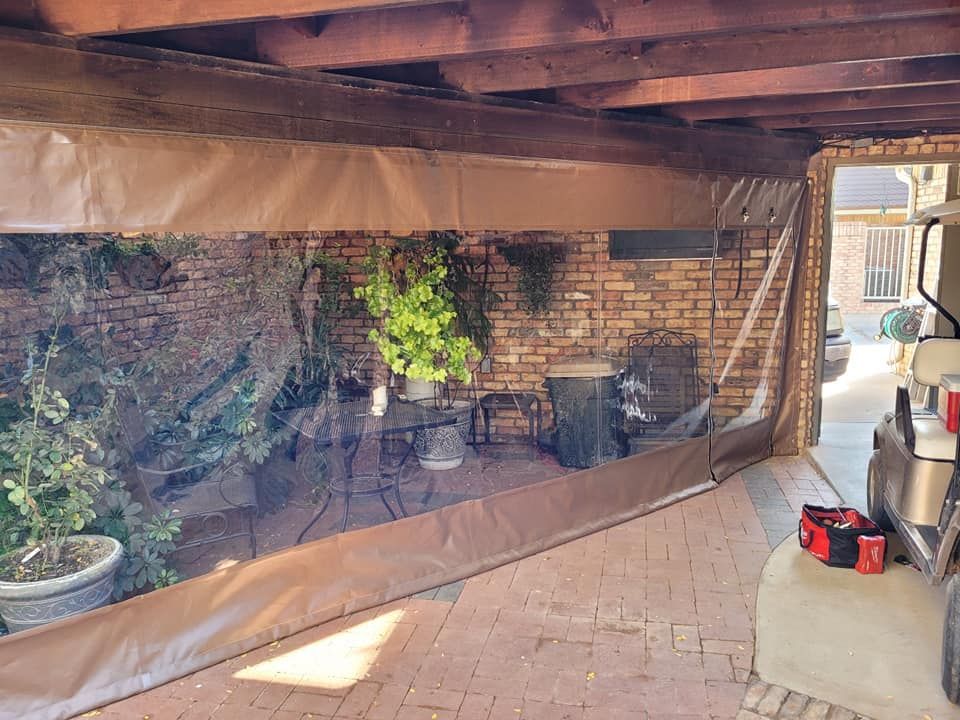Clear plastic and brown fabric enclosure added to a brick wall under a wooden overhang. Plants and a golf cart are visible.
