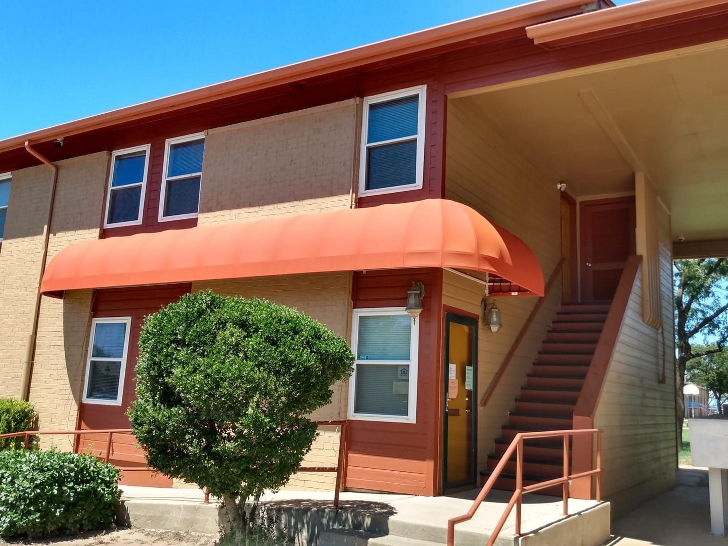 Two-story tan and brown building with red awning over a door, outdoor stairs to upper level.
