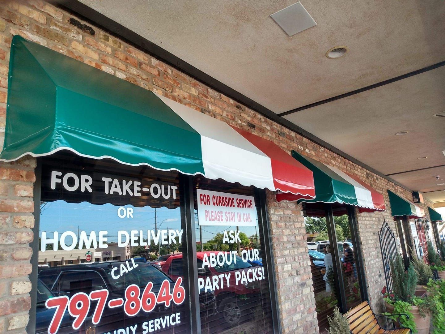 Restaurant exterior with green, white, and red awnings over windows with take-out and party pack signage.
