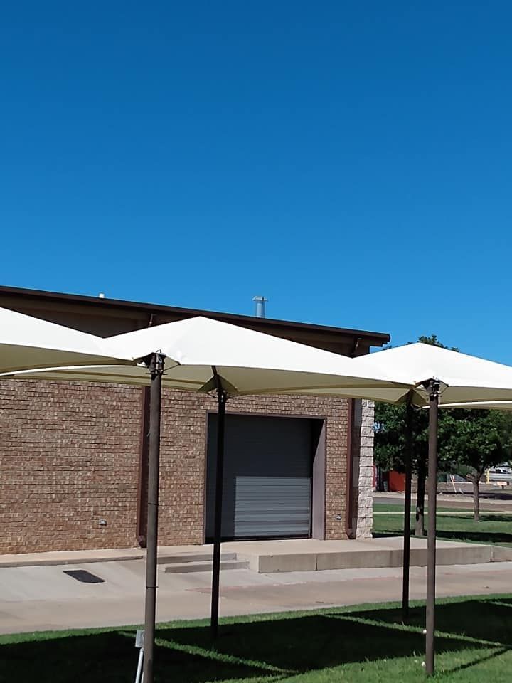 Building with brick facade and roll-up door, shaded by beige square umbrellas on a sunny day.