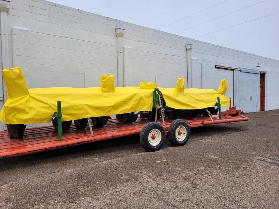 A yellow-covered farm implement on a red trailer with white-wheeled tires, parked in front of a white building.