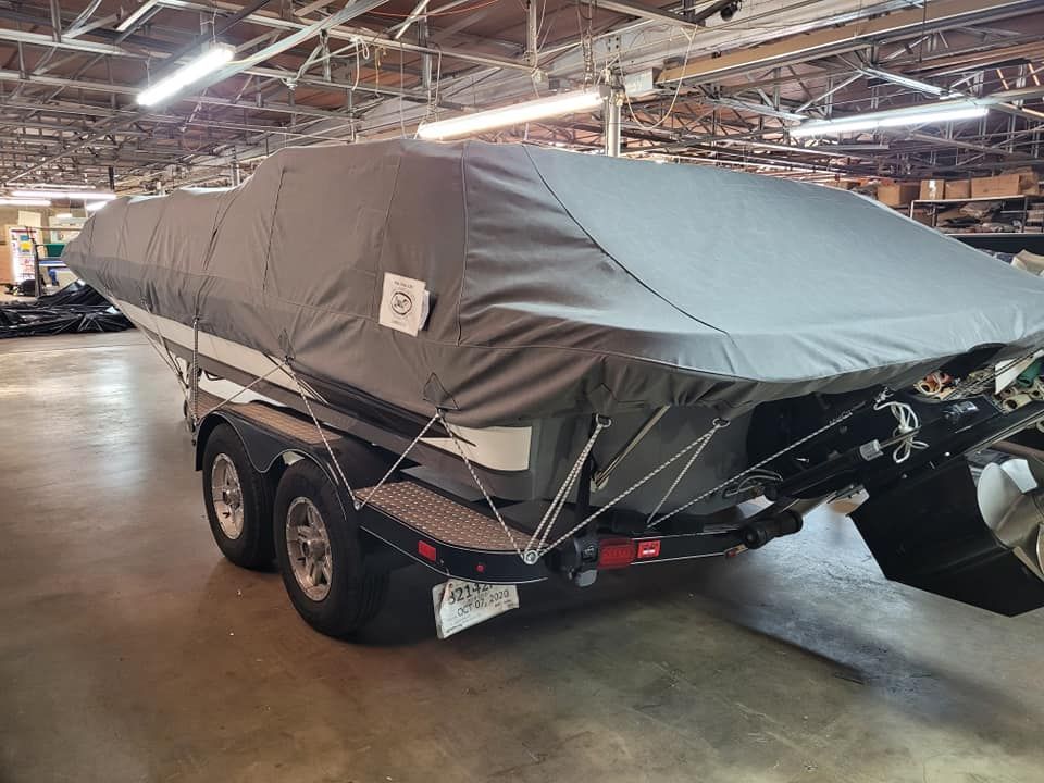Boat covered with a gray tarp on a trailer inside a building.