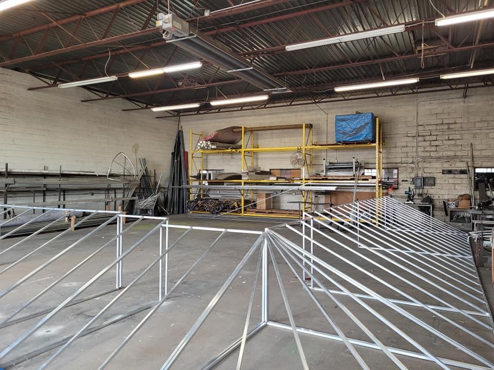 Metal framework in workshop. Yellow shelving holds various items. Gray concrete floor.