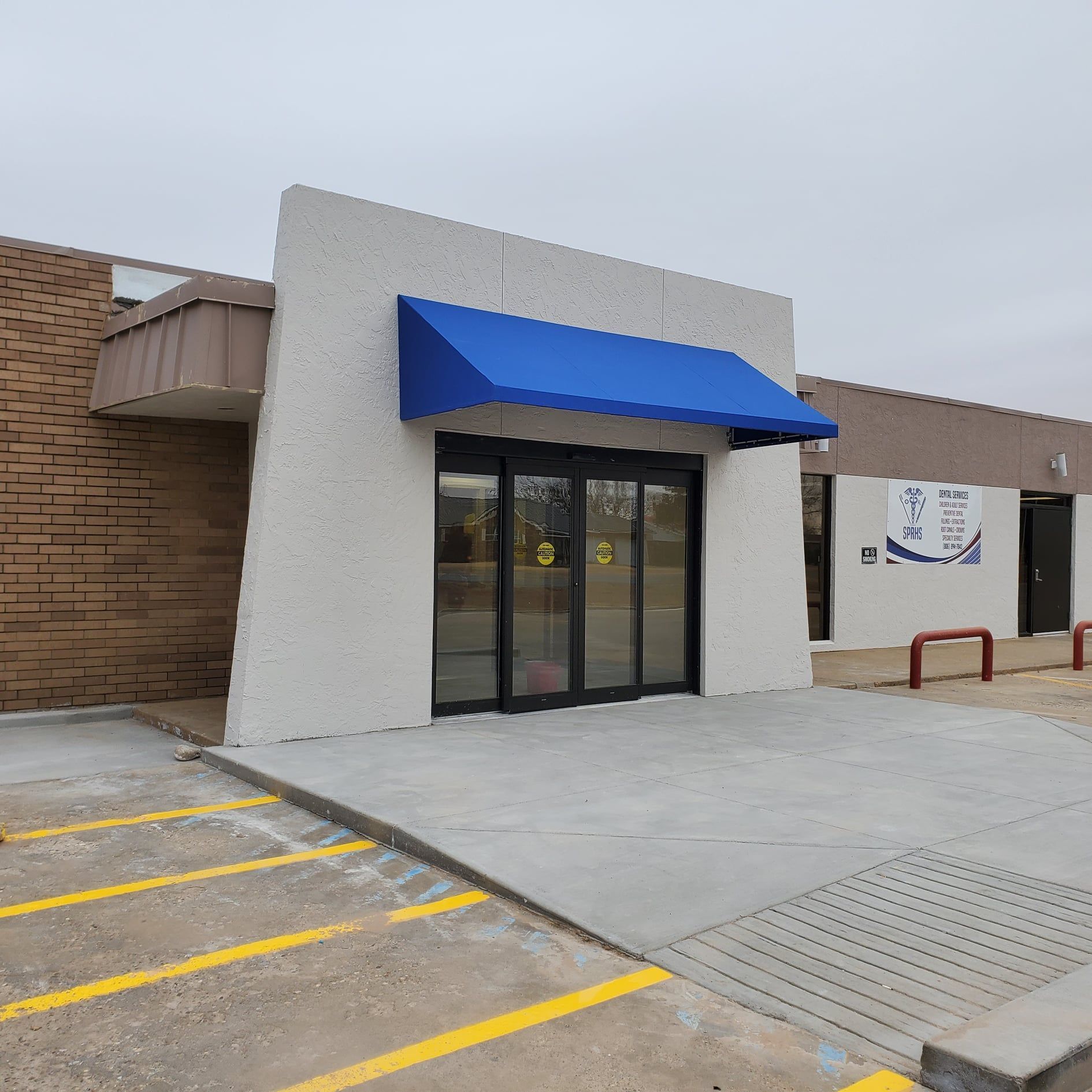 Exterior of a building with blue awning over glass doors and a concrete ramp for accessibility.