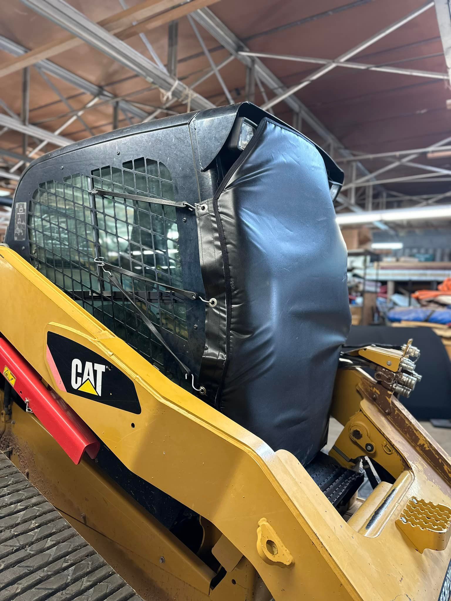 Yellow Caterpillar skid steer with black cover on cab, inside a building.