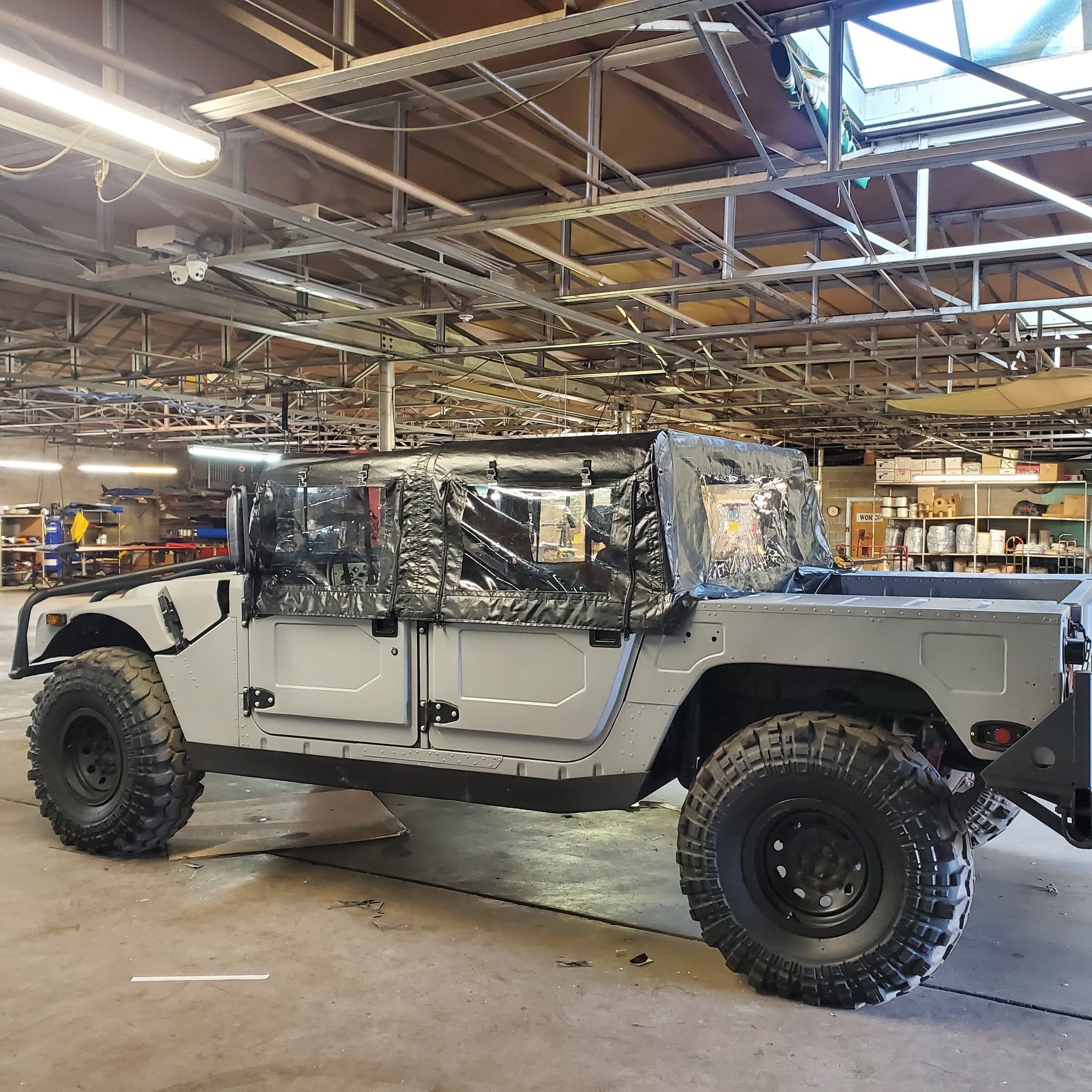 Gray Humvee with black tires and a soft top in a workshop setting.