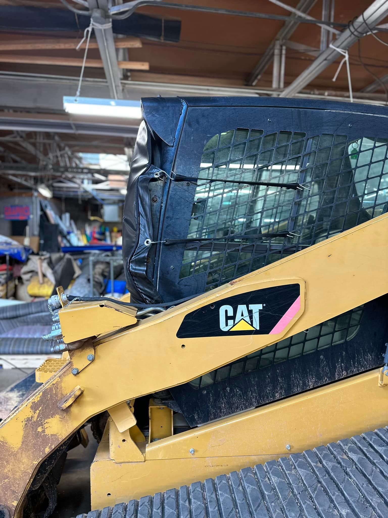Yellow Caterpillar skid steer with black cab in a warehouse.