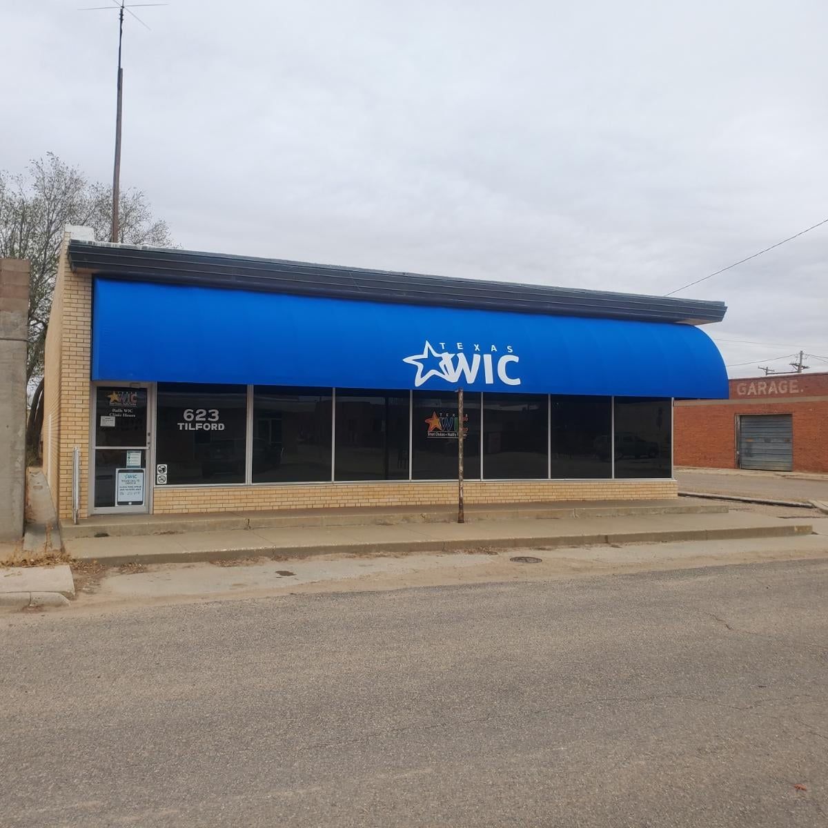 A storefront with a blue awning displaying the WIC logo. The building is brick with large windows.