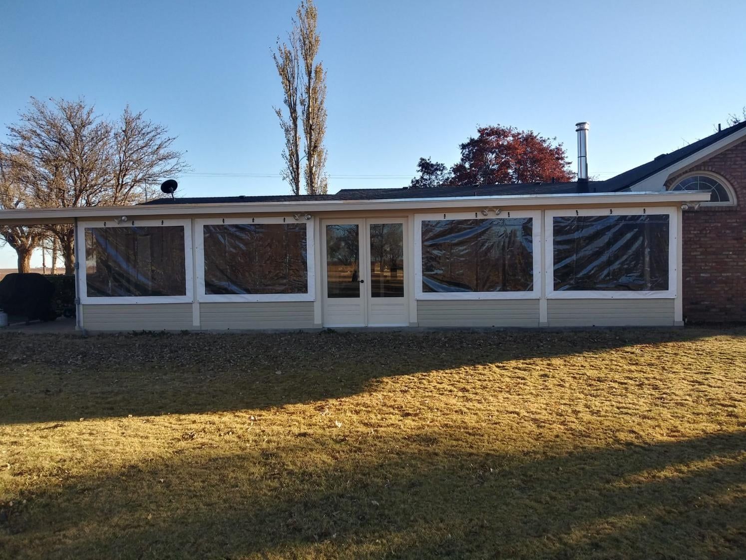 Sunroom with clear plastic coverings. Beige walls and a door. Located in front of a lawn.