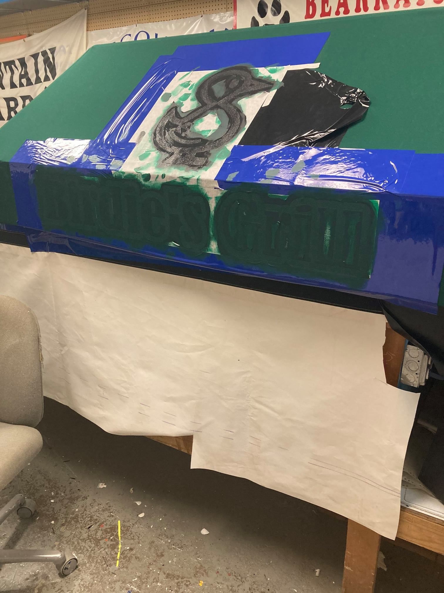 Green and blue painted object with a black logo, sitting on a table covered in white paper.