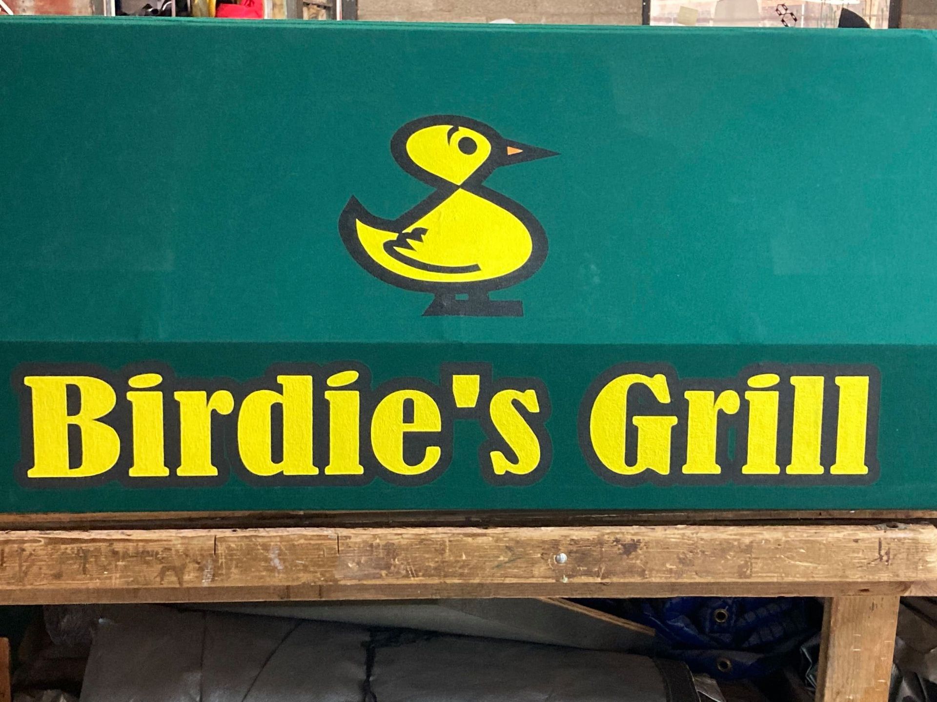 Birdie's Grill sign with a yellow duck logo on green background, yellow text on a wooden surface.