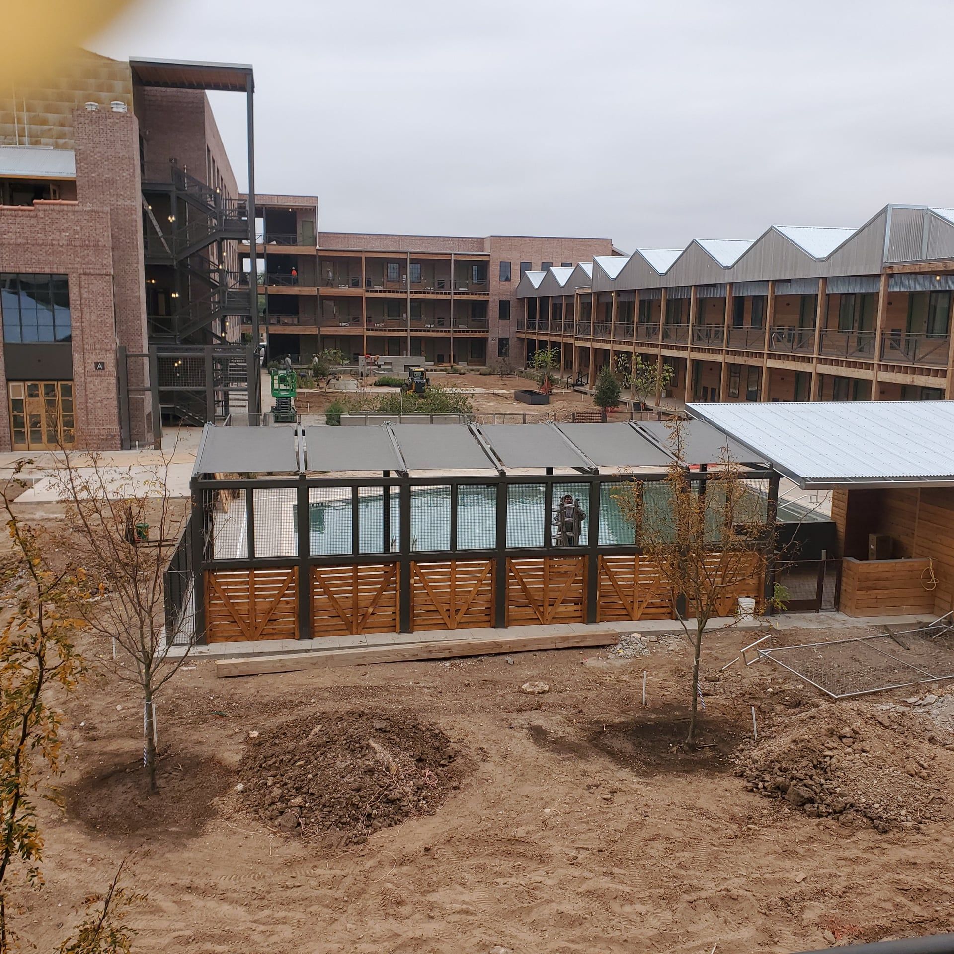 Outdoor pool with wooden enclosure in a courtyard of a brick building on an overcast day.