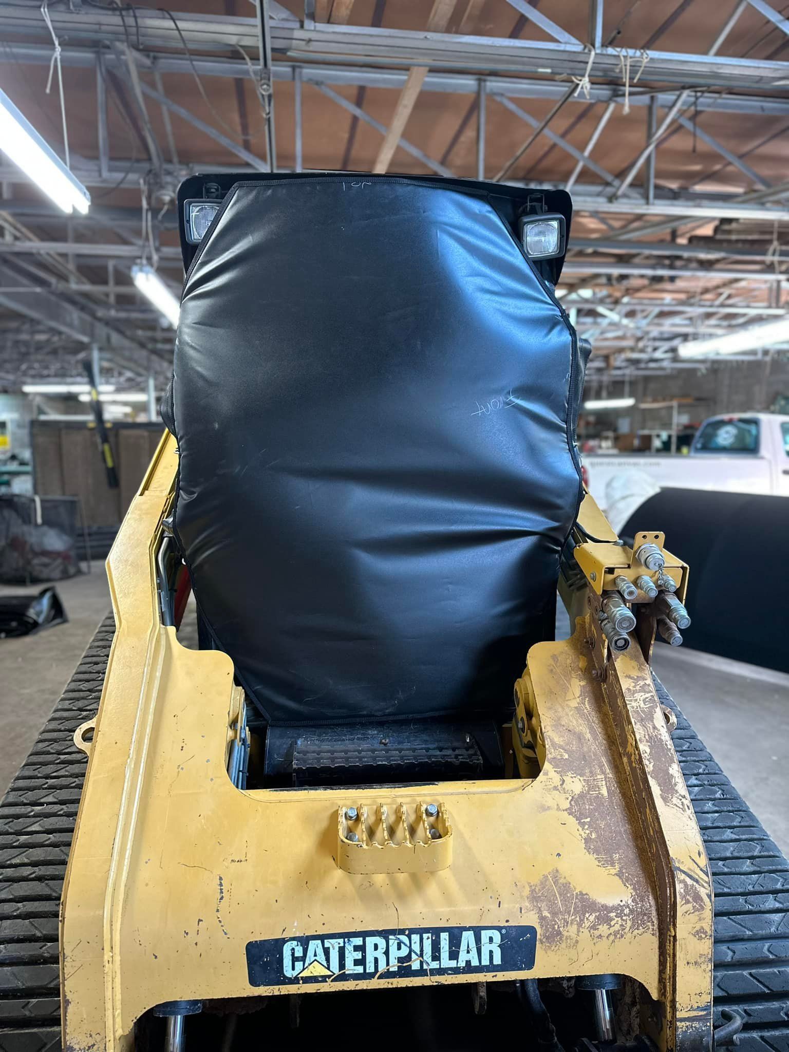 Yellow Caterpillar skid steer with a black covering. In an indoor setting.