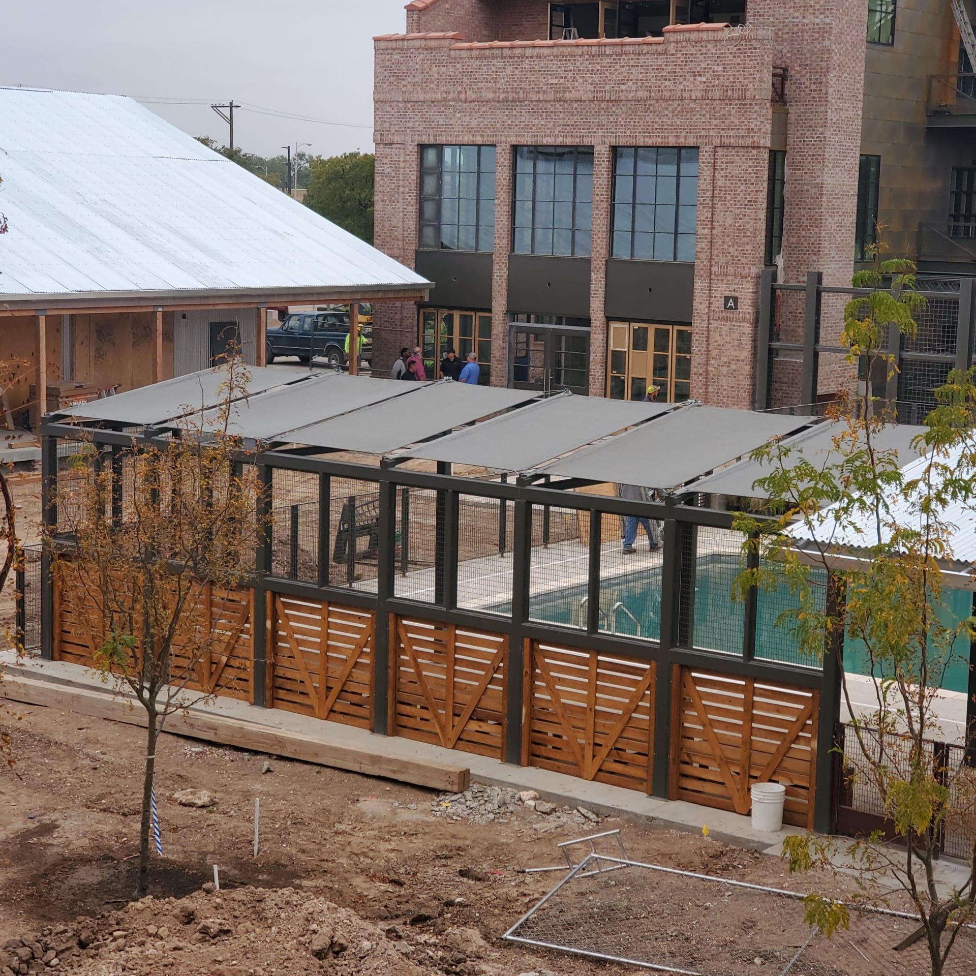Poolside canopy with wooden fence, and brick building in the background.