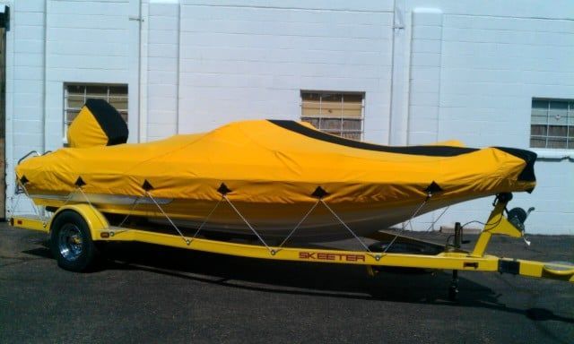 Yellow boat cover on a trailer, black accents. Outdoors, near a white building.