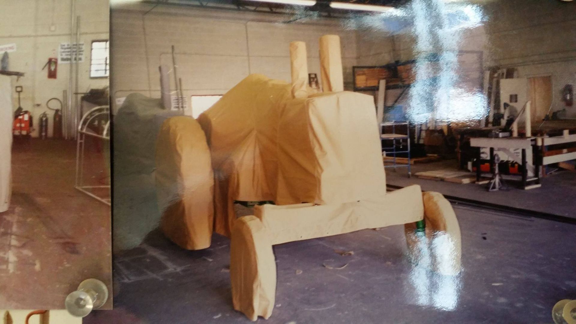 Wooden tractor model wrapped in yellow fabric, in a workshop.