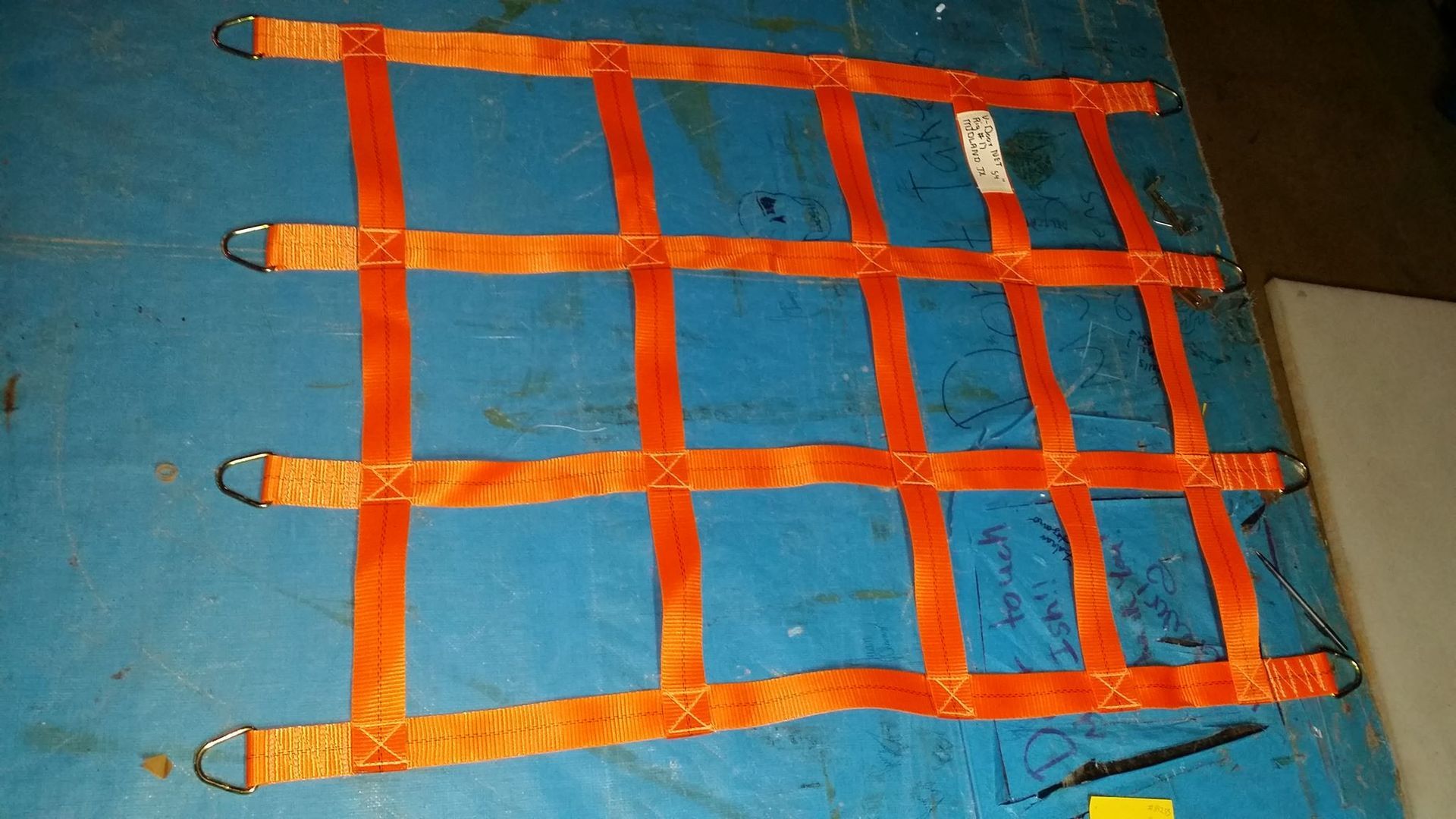 Orange cargo net with metal rings, lying on a blue surface.