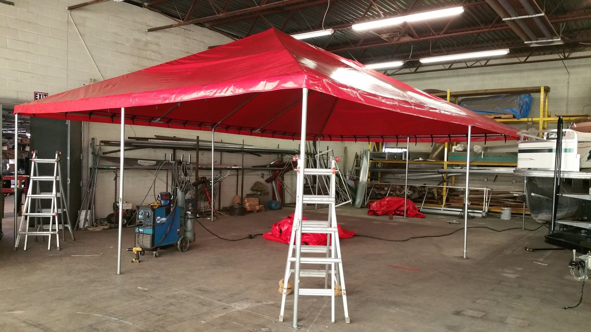 Red canopy tent set up inside a warehouse. Ladder in front.