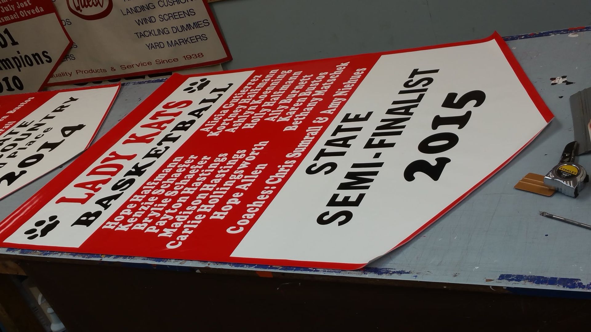 Red and white sign for Lady Kats Basketball, State Semi-Finalist 2015. Lists players, coaches.