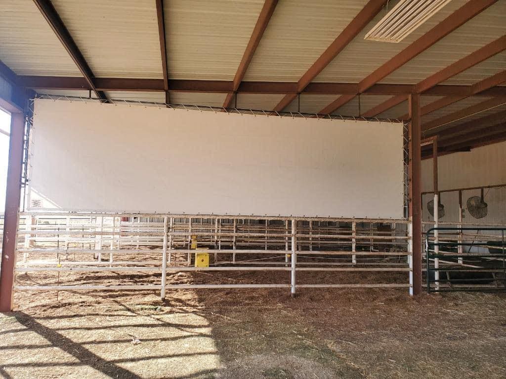 Large white screen hanging in a metal-framed barn. Metal cattle pens are visible behind it.
