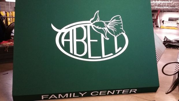 Green sign with "Abell Family Center" in white lettering and logo of an oval with bow-like design.