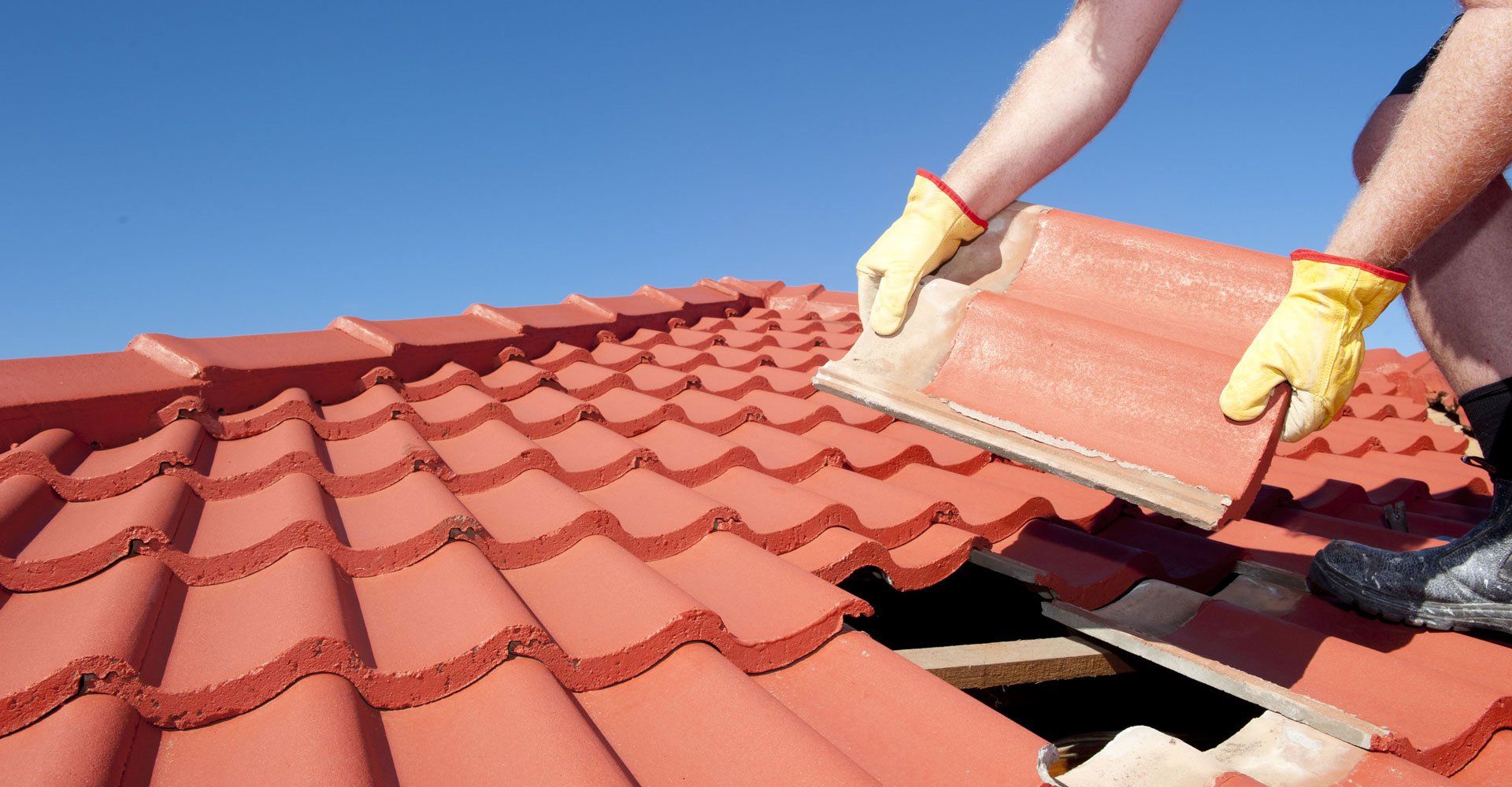 Roof repair, worker with yellow gloves replacing red tiles