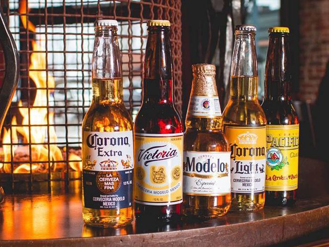 Five beer bottles lined up on a bar, with a fire pit in the background