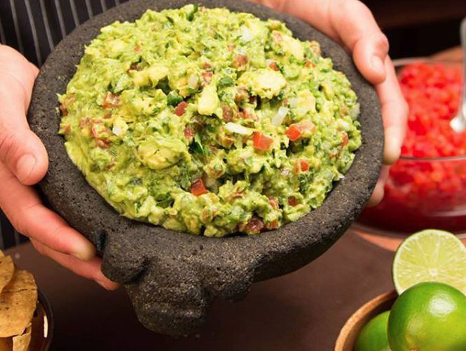 Hands holding a molcajete filled with fresh guacamole