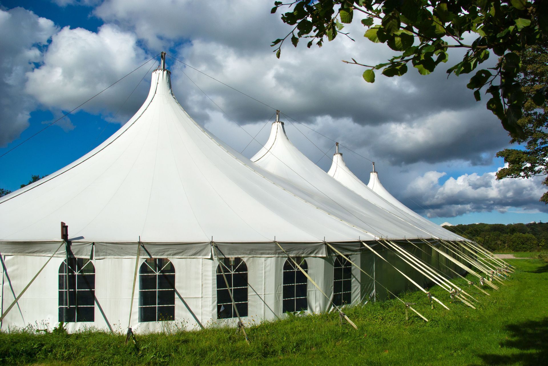 White, peaked tents in a green field under a blue sky with fluffy clouds.